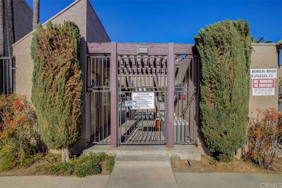 Front view of a gated entrance to a building with tall hedges on either side.