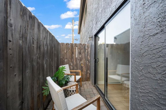 Narrow outdoor patio area with a wooden fence and sliding glass doors.