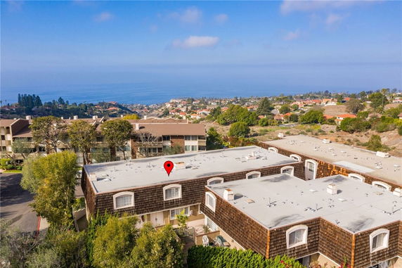 Aerial view of buildings with ocean and hilly terrain in the background.