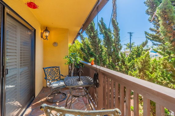 Outdoor balcony area with a small table, chairs, and view of nearby trees.