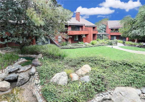 Front view of a two-story brick house with a chimney and surrounding greenery.