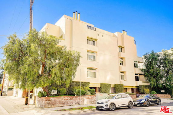 Front view of a multi-story building with balconies and trees in front.