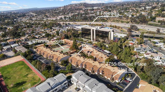 Panoramic view of a residential complex with tennis courts, swimming pool, and nearby freeway.