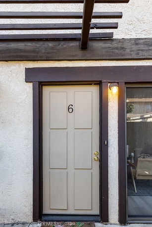 Front view of a door with number 6 under a wooden pergola.