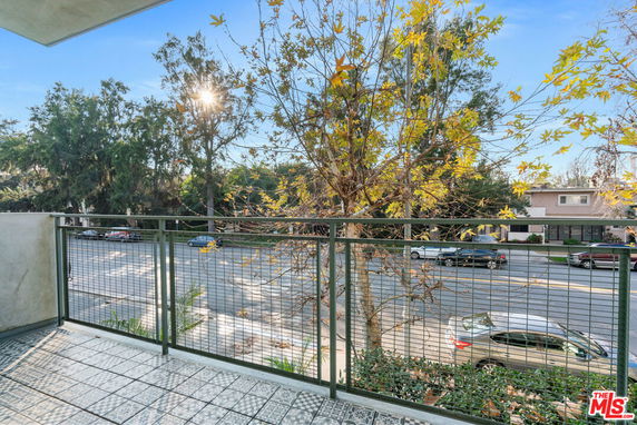 View from a balcony overlooking a street with cars and leafy trees.