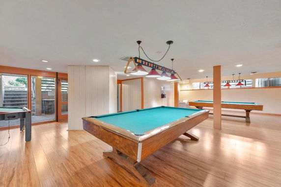Indoor recreational area with multiple pool tables and wooden flooring.