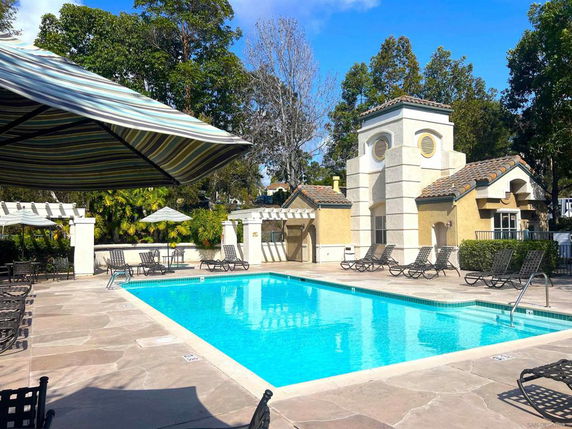 Outdoor swimming pool area with seating and a small building.