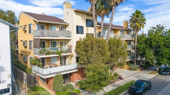 Front view of a multi-story residential building with balconies and surrounding trees.