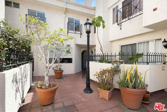 Patio area of a building with potted plants and decorative metal fencing.