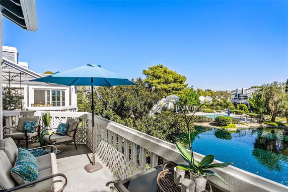 Balcony with seating and umbrella overlooking a pond and lush greenery.
