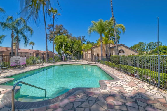 Outdoor swimming pool surrounded by a paved area and palm trees.