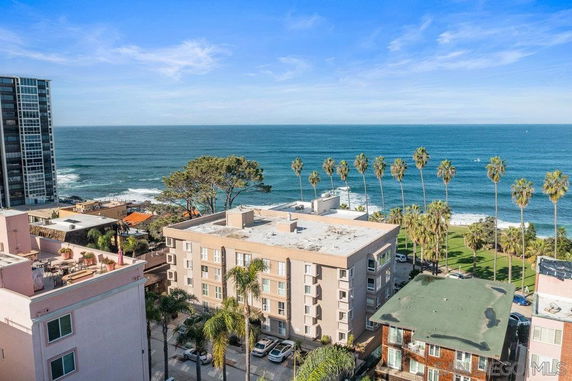 Panoramic view of oceanfront buildings with palm trees and ocean in the background.