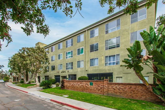 Front view of a multi-story apartment building with green facade and several windows.