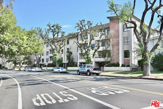 Front view of a multi-story residential building with trees and parked cars.
