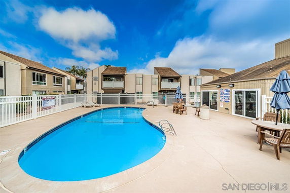 Outdoor area with a swimming pool surrounded by buildings and fenced with patio furniture.