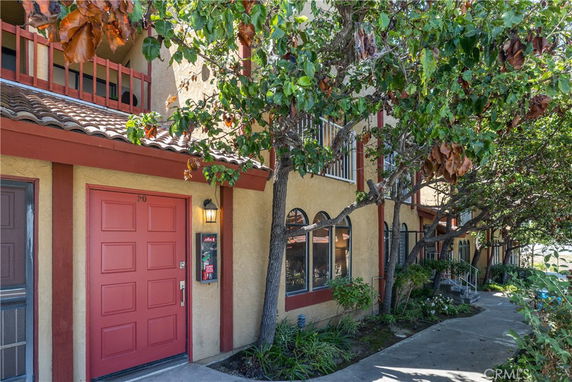 Front view of a multi-story building with a red door and arched windows, surrounded by trees and a walkway.