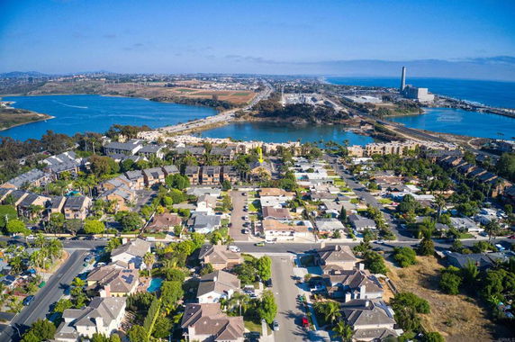 Aerial panoramic view of a residential area with roads, houses, and surrounding water bodies.