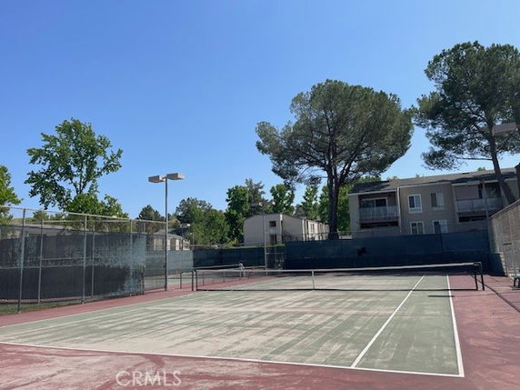 Tennis court with surrounding trees and buildings.