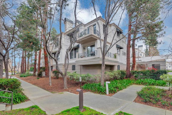 Front view of a multi-story residential building with balconies and trees nearby.