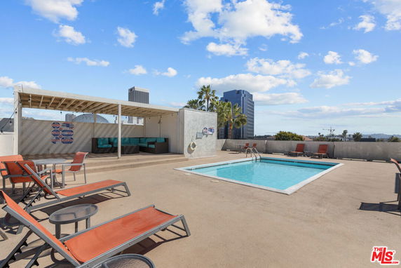 Rooftop view of a swimming pool with lounge chairs and seating area under a canopy.