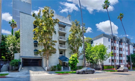 Front view of a multi-story building with balconies and a gated parking entry.