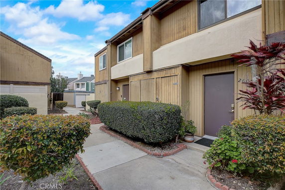 Front view of a two-story townhouse with a walkway and shrubs.