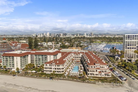 Aerial view of a beachfront hotel complex with red roofs overlooking the city skyline and marina.