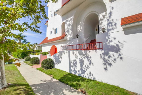 Front view of a multi-story building with white walls and red roof accents.