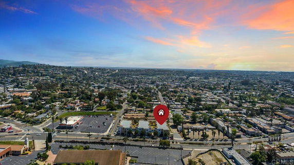 Wide aerial view of a suburban town with various buildings and roads under a colorful sky.