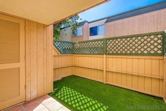 Small outdoor fenced area with artificial grass and wooden fence.
