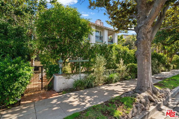 Front view of a two-story house with a gated entrance and lush greenery.