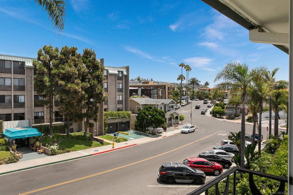 Street view with apartment buildings and parked cars, seen from a balcony.