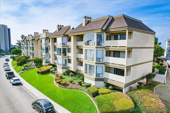 Front view of a multi-story apartment building with balconies and landscaped surroundings.