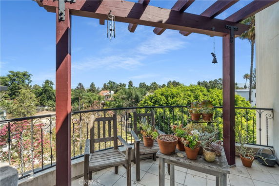 Balcony with potted plants and a chair overlooking trees and surrounding area.