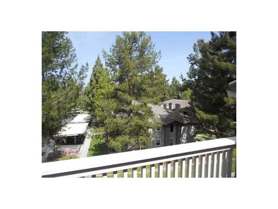View from a balcony showing surrounding trees and a residential building.