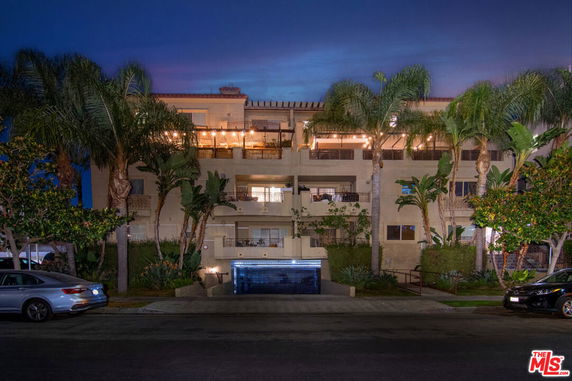 Front view of a multi-story building at night with palm trees and lights.