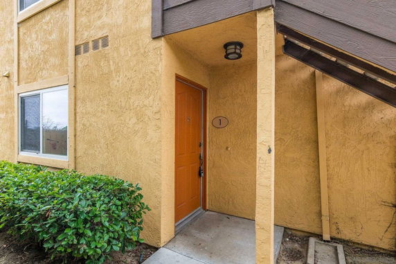 Front view of an apartment entrance with an orange door and number, under a set of stairs.