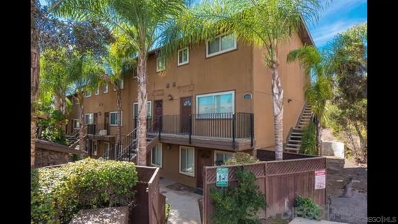 Front view of a multi-story apartment building with external staircases and palm trees.