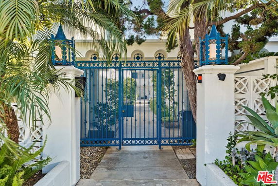Front view of a house gate with blue ornate design and white pillars.