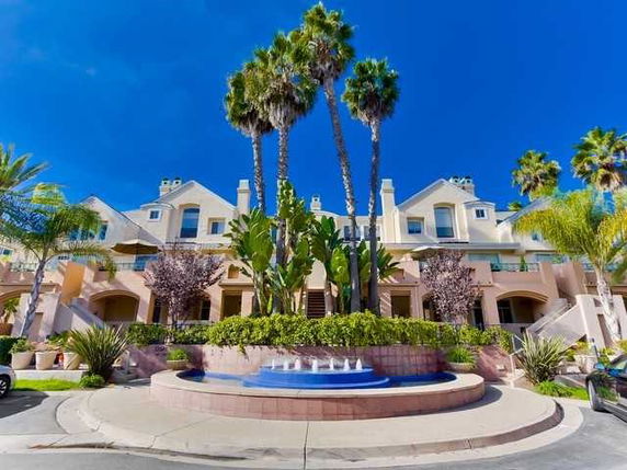 Front view of a multi-story house with a central fountain and palm trees.