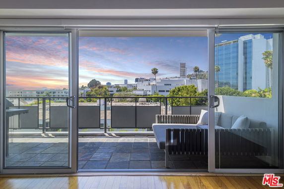 Panoramic view from a balcony with glass sliding doors, overlooking cityscape and distant buildings.