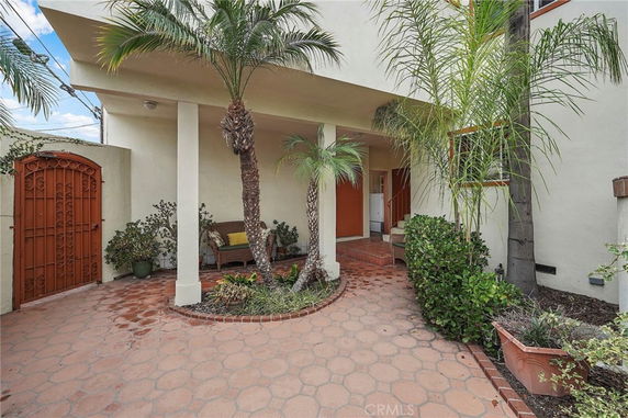 Front view of a house with a covered entrance and surrounding palm plants.
