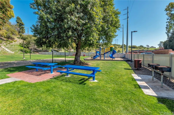 Outdoor play area with picnic tables, a barbecue grill, and a children's playground with slides.