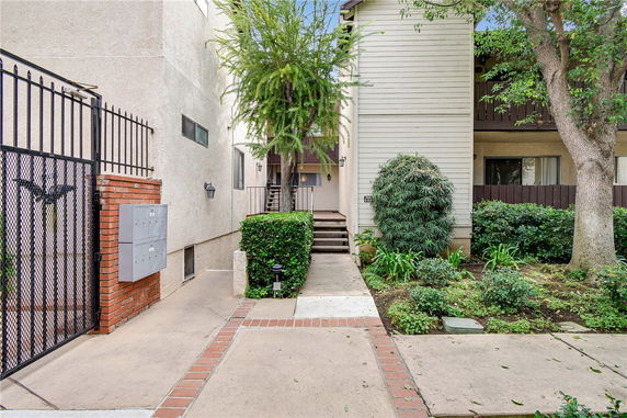 Front view of an apartment building entrance with stairway and landscaped pathway.