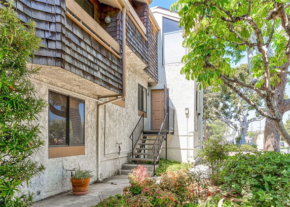 Front view of a multi-story residential building with wooden shingle siding and stairs leading to the entrance.