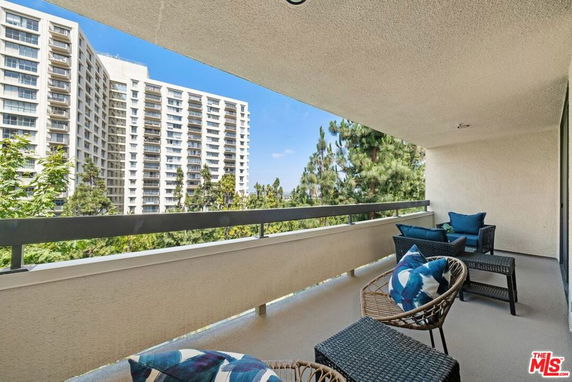 Balcony view with chairs, overlooking tall residential buildings and trees.