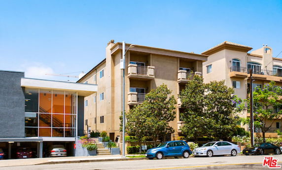 Front view of a multi-story apartment building with balconies and multiple cars parked in front.