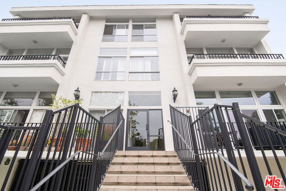 Front view of a multi-story building with balconies and stairs leading to the entrance.