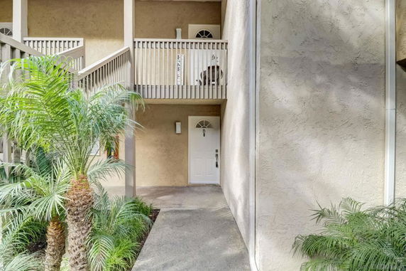 Exterior view of a multi-story building entrance with a balcony and plants.