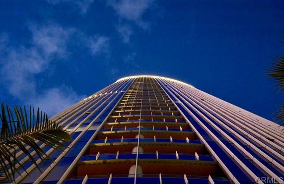 Upward view of a tall, modern skyscraper with illuminated upper floors against a dark blue sky.